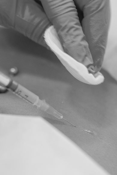 Primer plano de una mano con una jeringuilla y otra con un algodón