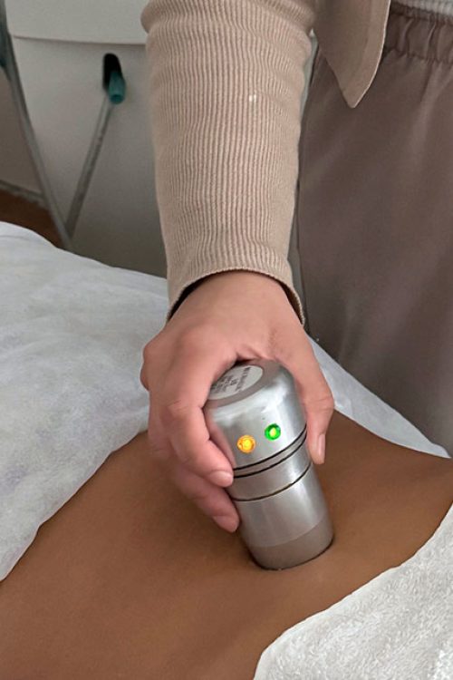 Una mano sosteniendo un pequeño aparato sobre la espalda de otra persona tumbada en una camilla